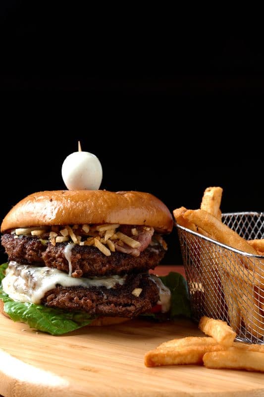 Gourmet double cheeseburger topped with a quail egg, served next to a basket of fries.