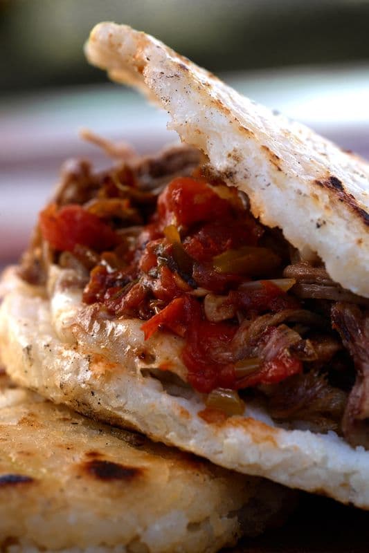 Close-up of a toasted arepa stuffed with shredded beef and a chunky tomato sauce.